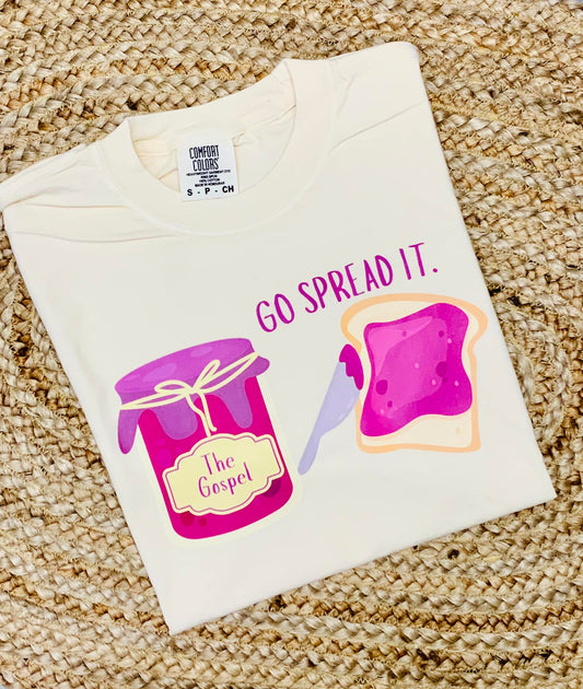 A youth-sized white t-shirt with a graphic print of a jar and a slice of bread, alongside the phrase 'GO SPREAD IT.'