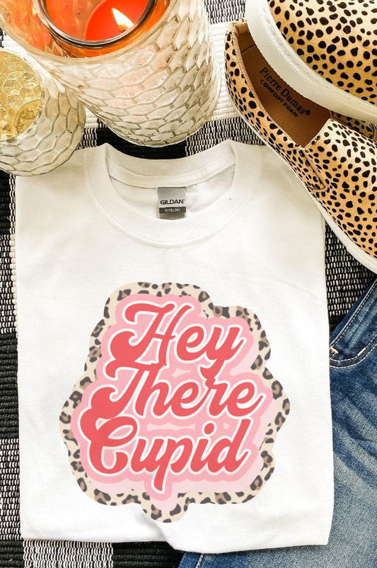White t-shirt with 'Hey There Cupid' design, leopard print shoes, and candle on a checkered fabric background