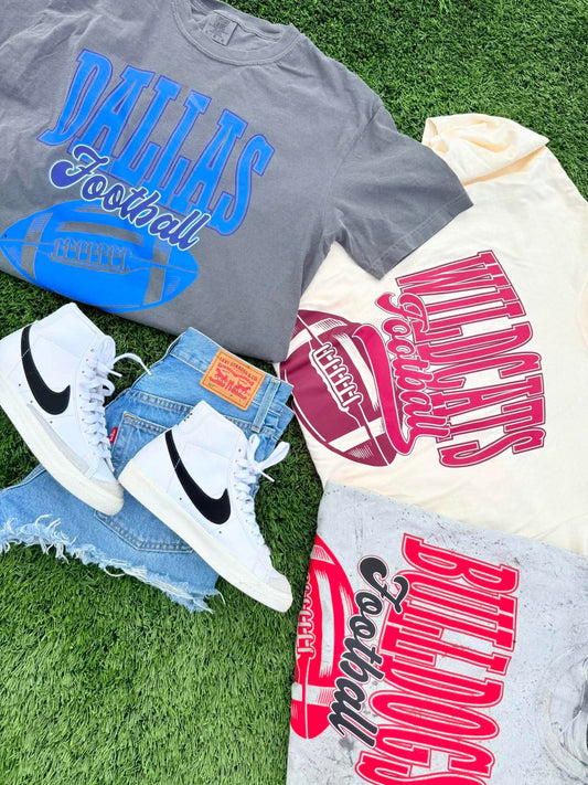 Gray t-shirt with 'Dallas Football' text, white sneakers, and denim shorts on grass.