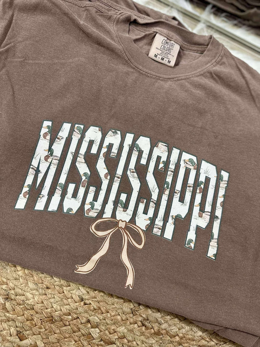 Brown t-shirt with 'Mississippi' printed on it, featuring a bow design, on a woven surface.